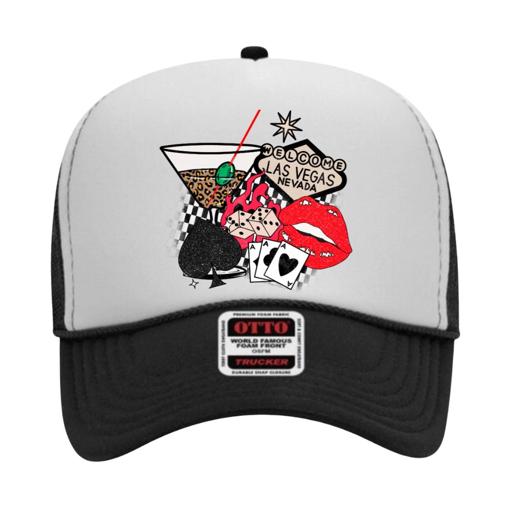 Trucker hat with bold Las Vegas-themed design featuring a martini, dice, cards, lips, and iconic sign on a white front and black mesh back.